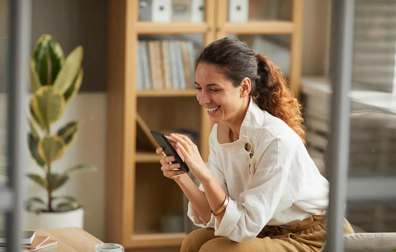 Vrouw lacht terwijl ze op haar smartphone kijkt in een moderne kantoorruimte, symbool voor professioneel en flexibel werken met een virtueel kantoor.
