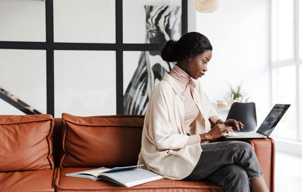 Vrouw werkt op laptop in een moderne, lichte kantoorruimte met open boek op een leren bank.