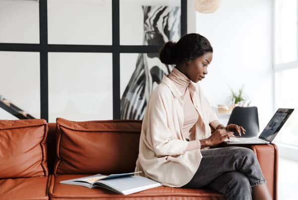 Vrouw werkt op laptop in een moderne, lichte kantoorruimte met open boek op een leren bank.