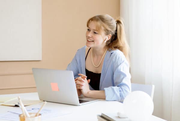 Een vriendelijke vrouw die met haar handen in elkaar zit achter haar laptop. Ze praat op een vriendelijke manier met de persoon die tegenover haar zit.