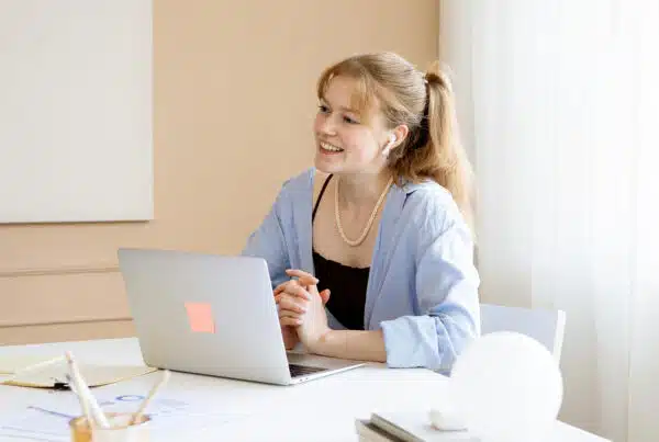 Een vriendelijke vrouw die met haar handen in elkaar zit achter haar laptop. Ze praat op een vriendelijke manier met de persoon die tegenover haar zit.