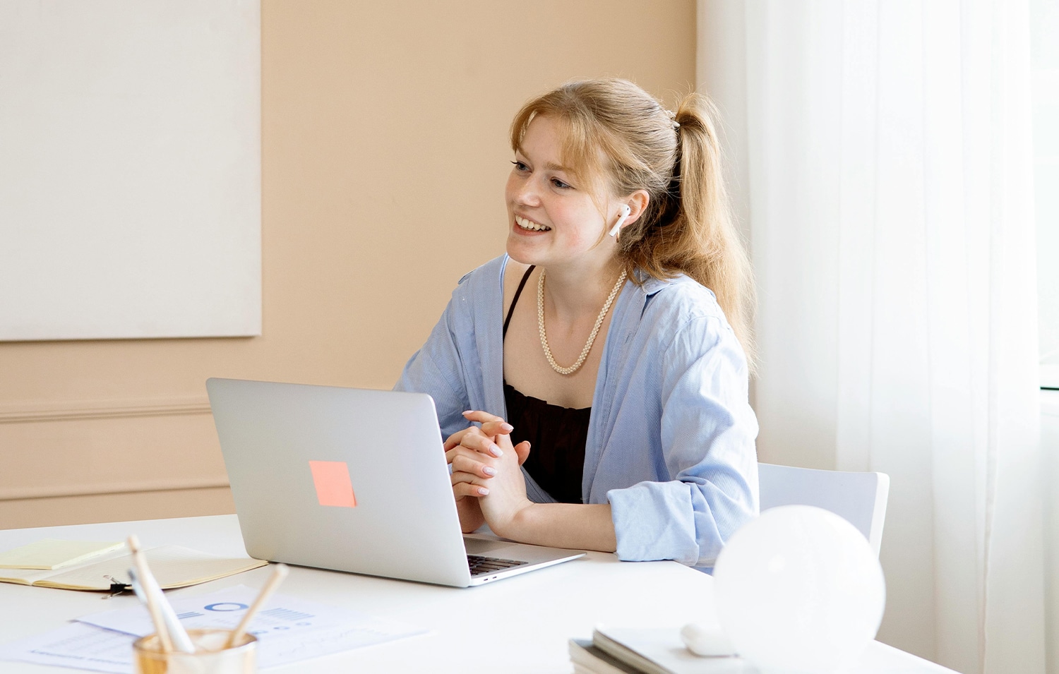 Een vriendelijke vrouw die met haar handen in elkaar zit achter haar laptop. Ze praat op een vriendelijke manier met de persoon die tegenover haar zit.