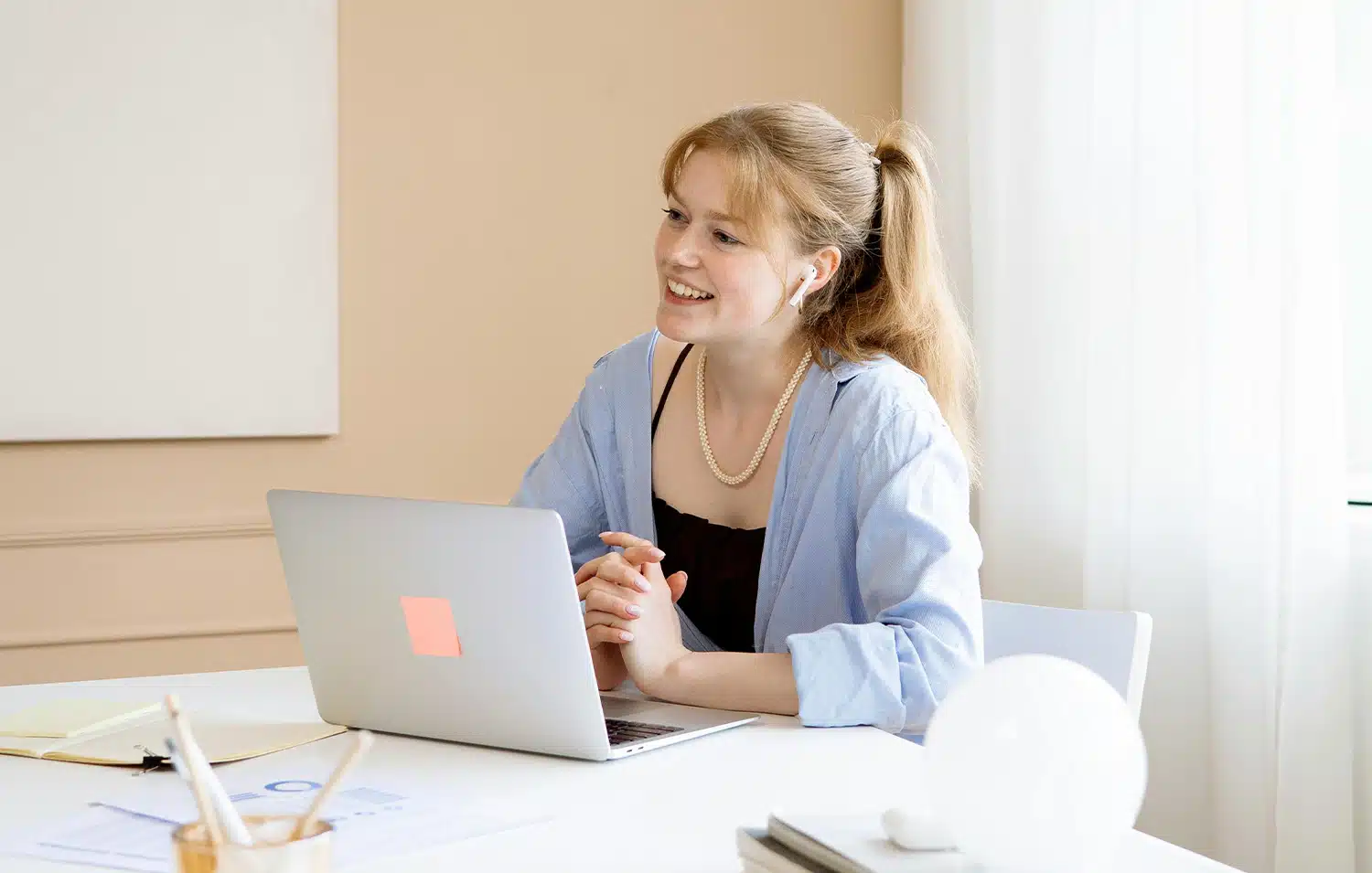 Een vriendelijke vrouw die met haar handen in elkaar zit achter haar laptop. Ze praat op een vriendelijke manier met de persoon die tegenover haar zit.