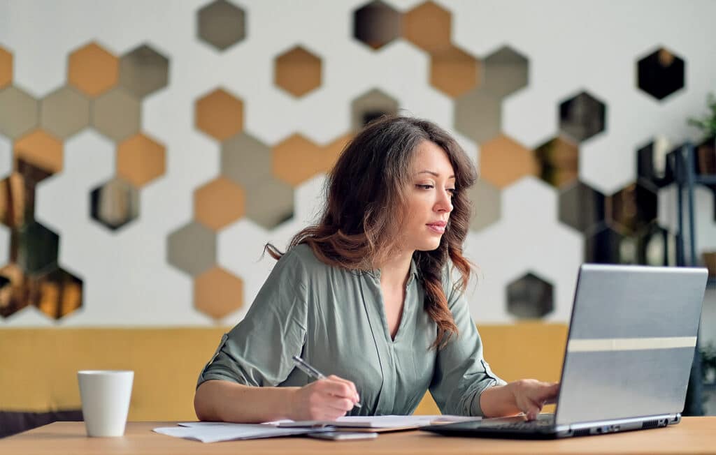 Vrouw is aan het ondernemen en werkt geconcentreerd op haar laptop aan een tafel.