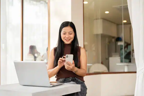 A satisfied Asian woman checks messages on her smartphone while working remotely from a coffee shop.